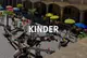 Schriftgrafik: Kinder. Dahinter ein Hof mit spielenden Kindern und bunten Sonnenschirmen.