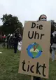 Demonstrantin hält in ihrer Hand ein selbst gemaltes Schild mit der Aufschrift „Die Uhr tickt“ und einem Globus, der gleichzeitig eine Uhr ist.